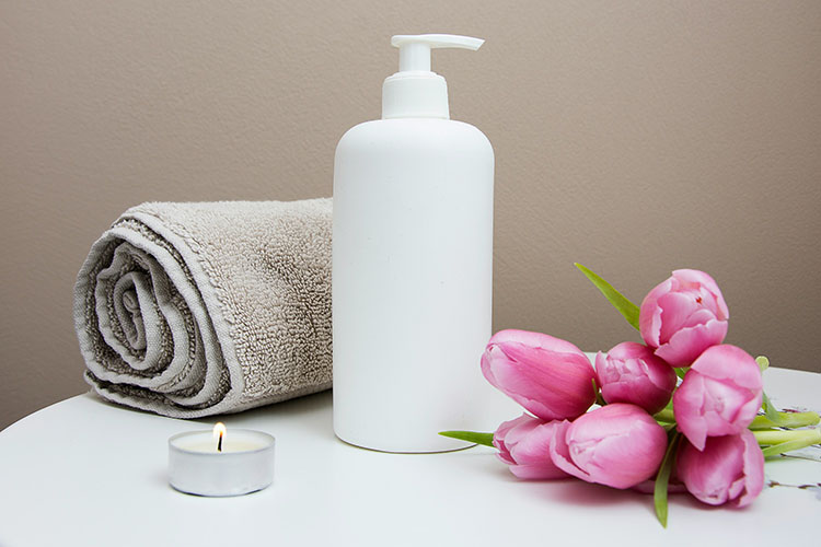 A small towel rolled up with an oil bottle, a lit tea light and a flower